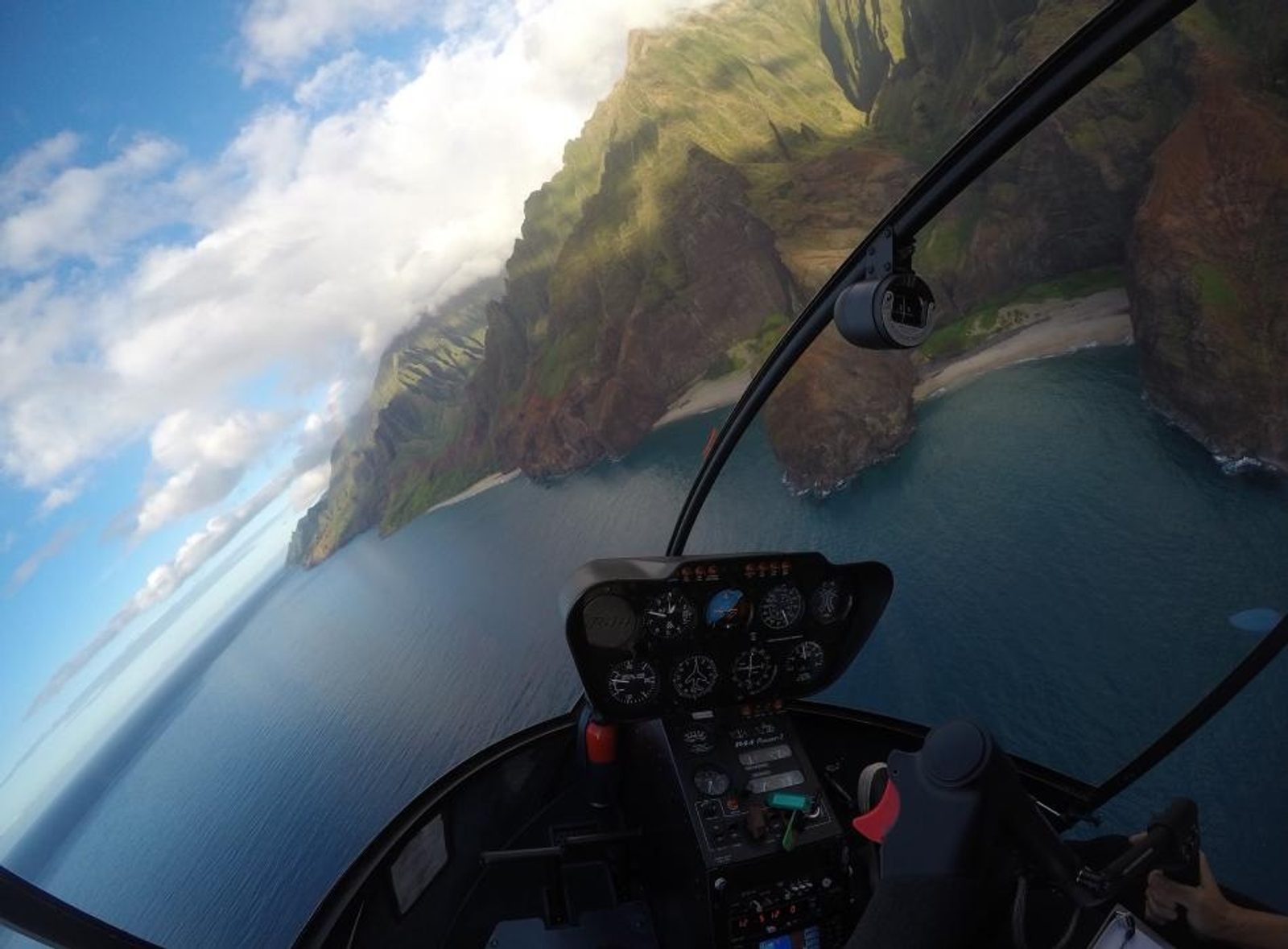 The view through the helicopter's bubble canopy over the pilot's shoulder of the Nā Pali cliffs and a white beach below