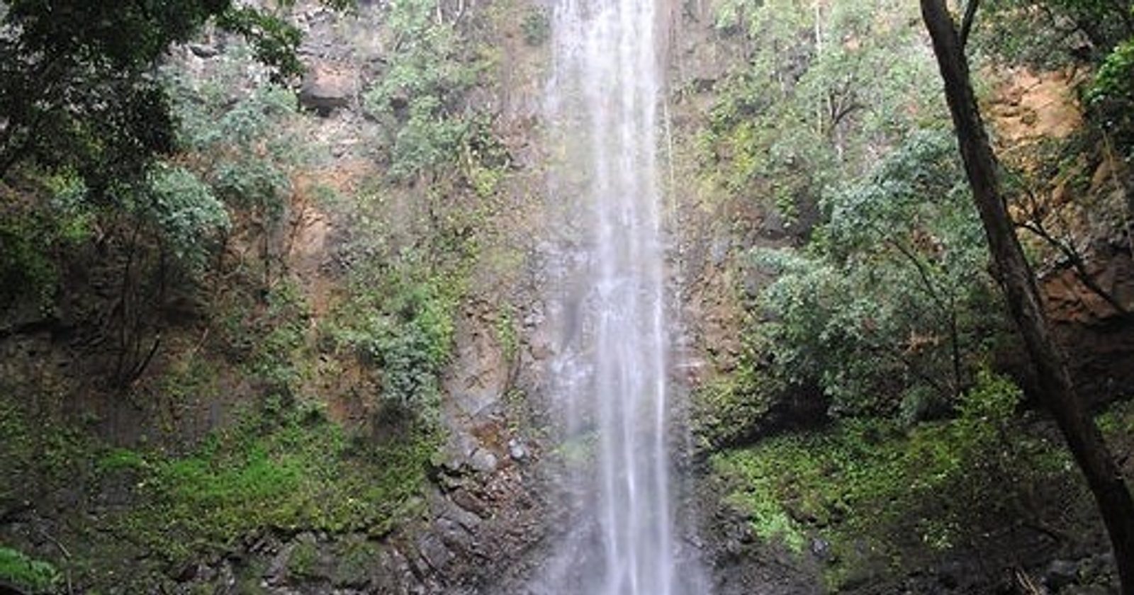 The full height of Secret Falls seen from the trail, with a hiker small at its base
