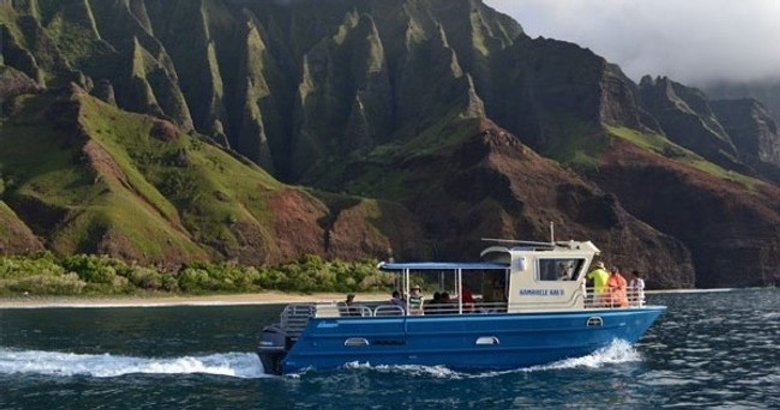The catamaran running along the base of the Nā Pali cliffs with mist on the upper ridges