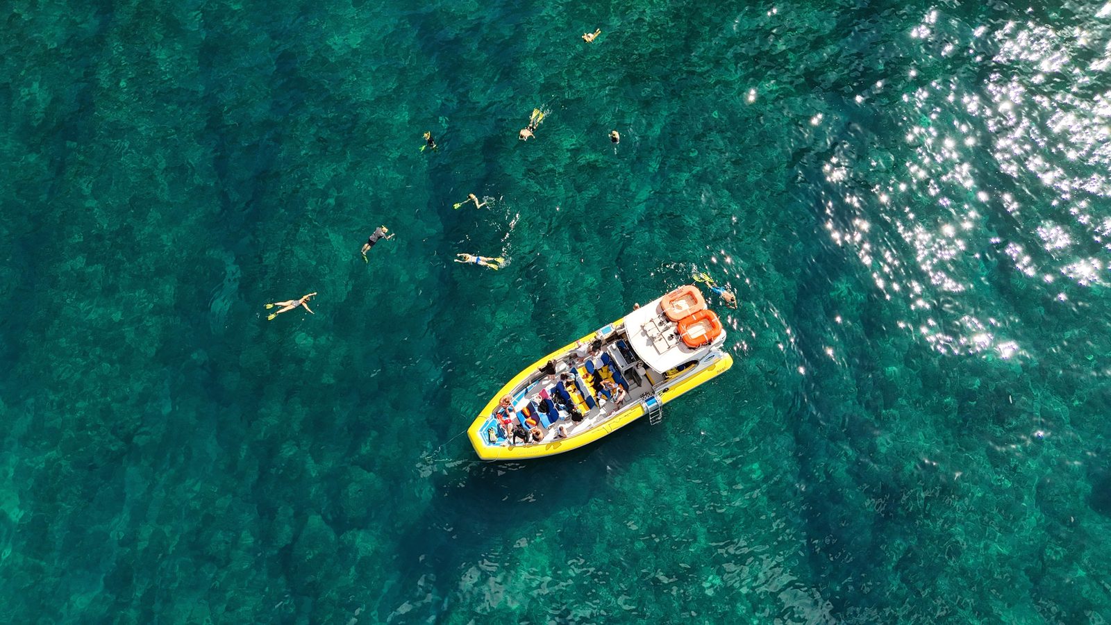 Aerial view of the raft anchored over a green reef with snorkelers spread out in the clear water around it