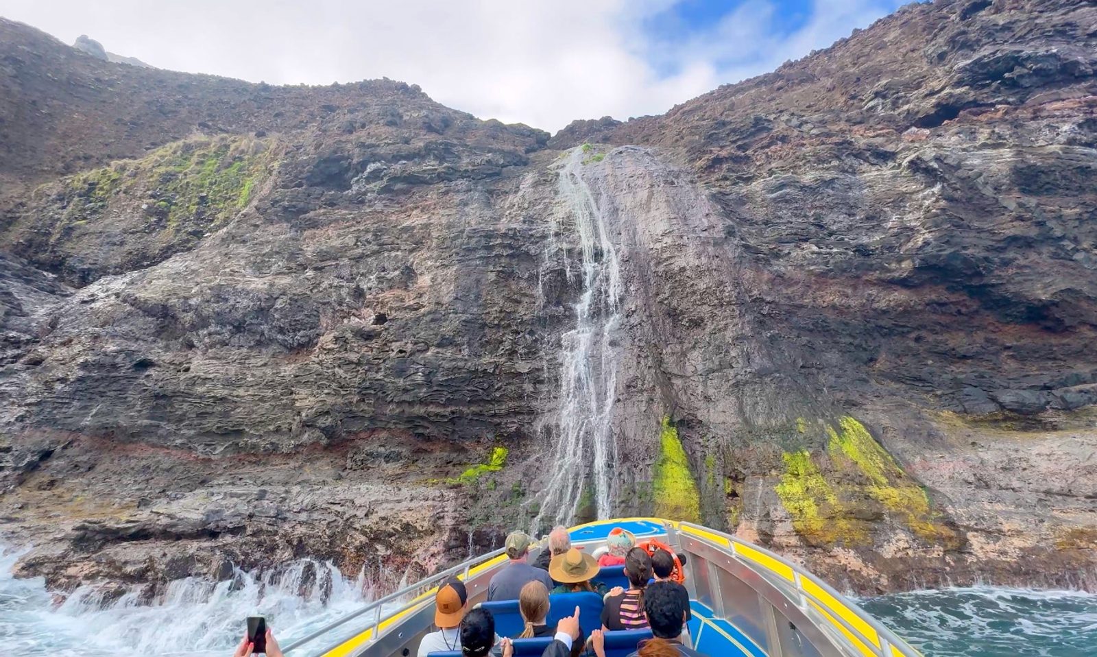Guests on the raft looking up at a tall waterfall streaming down a dark cliff face