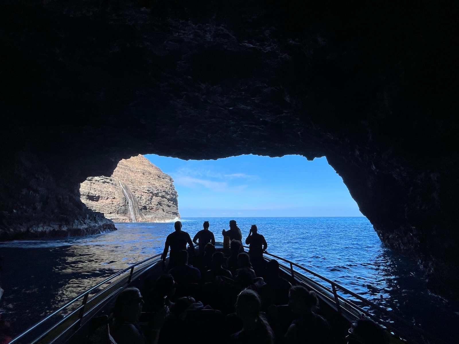 The view from inside a sea cave looking out past the silhouettes of guests to the bright ocean beyond