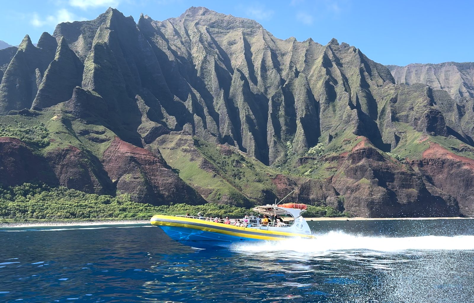 The raft at speed along the base of the Nā Pali cliffs, throwing a white wake