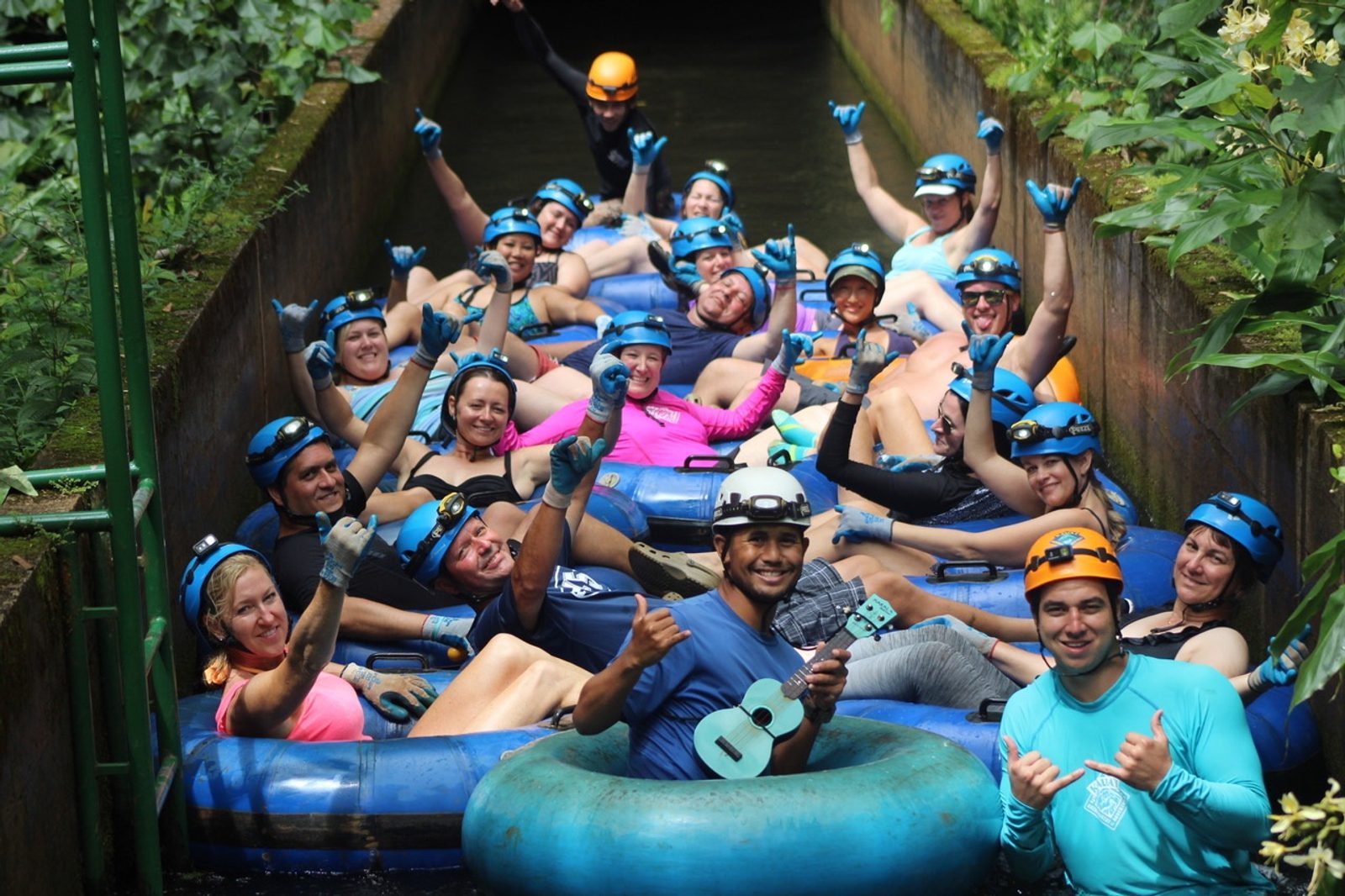 A large group of tubers in helmets and gloves raising their arms as they bunch up at the mouth of a stone tunnel